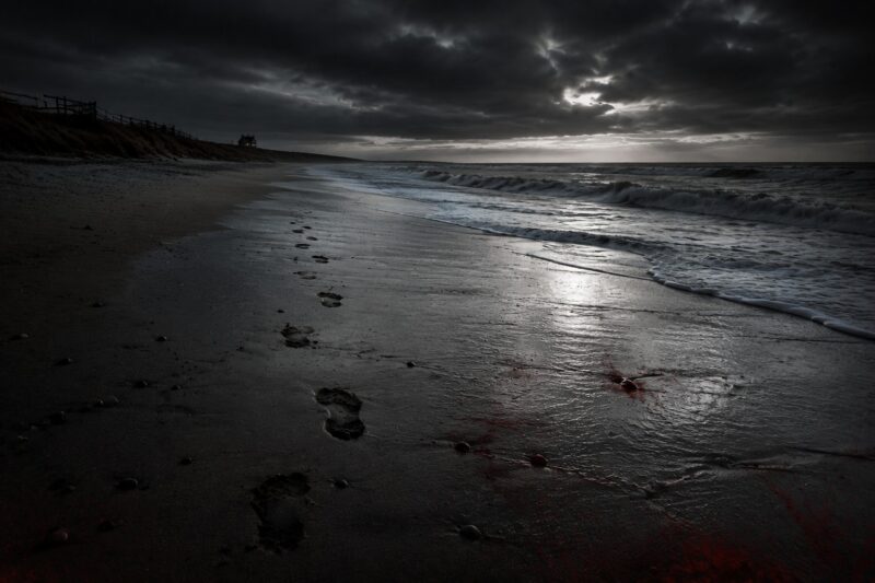 Atmospheric empty beach scene symbolising trauma and aftermath in Blood Ribbon by Roger Bray, a psychological thriller about survival and hidden danger.